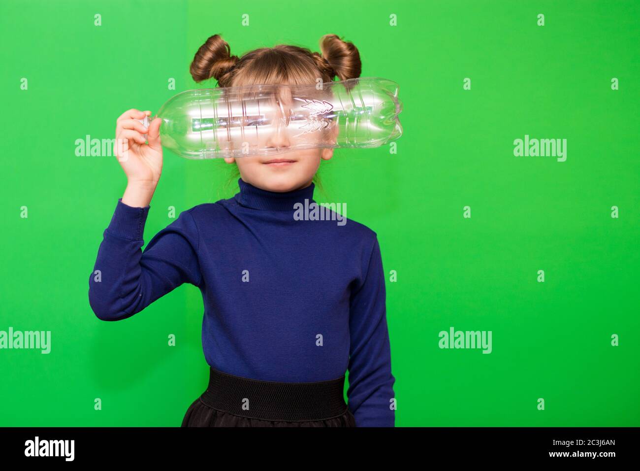 Little environmentalist girl isolated on green background looking through plastic bottle and shows interest in reducing plastic consumption and introd Stock Photo