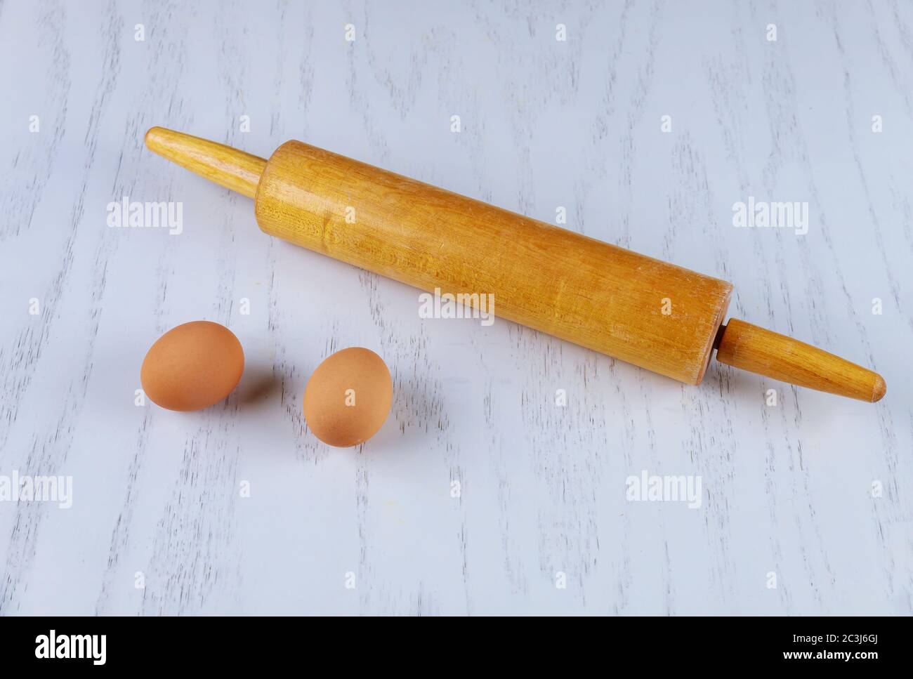 Rolling pin and two brown eggs on white table. Stock Photo