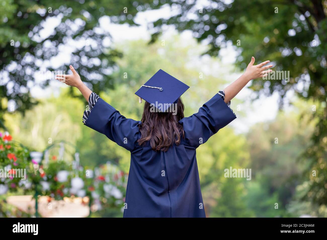 Back view of young woman graduating put her hands up and celebrating feeling so happy. Stock Photo
