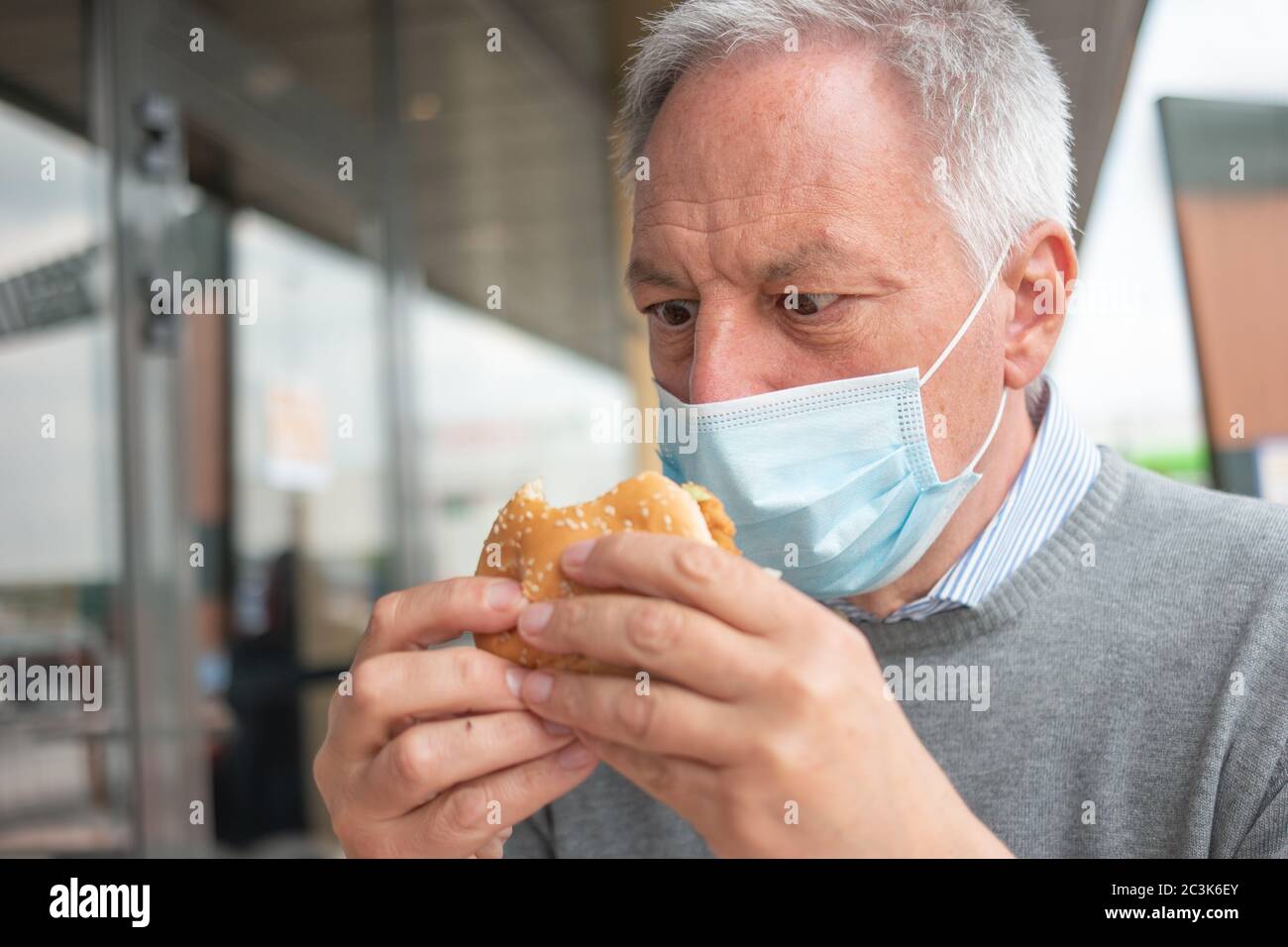 Man trying to eat his fast food lunch hamburger while wearing a mask
