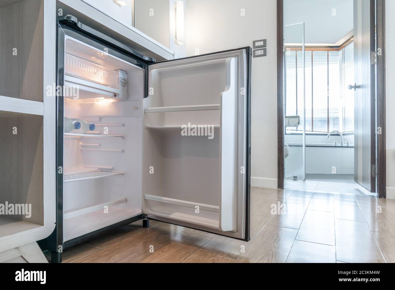 opened small refrigerator under the counter and in front of toilet in