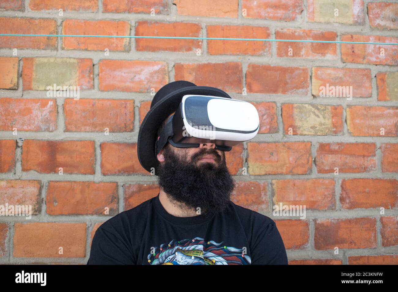 Bearded man wearing VR glasses, standing by a brick wall Stock Photo