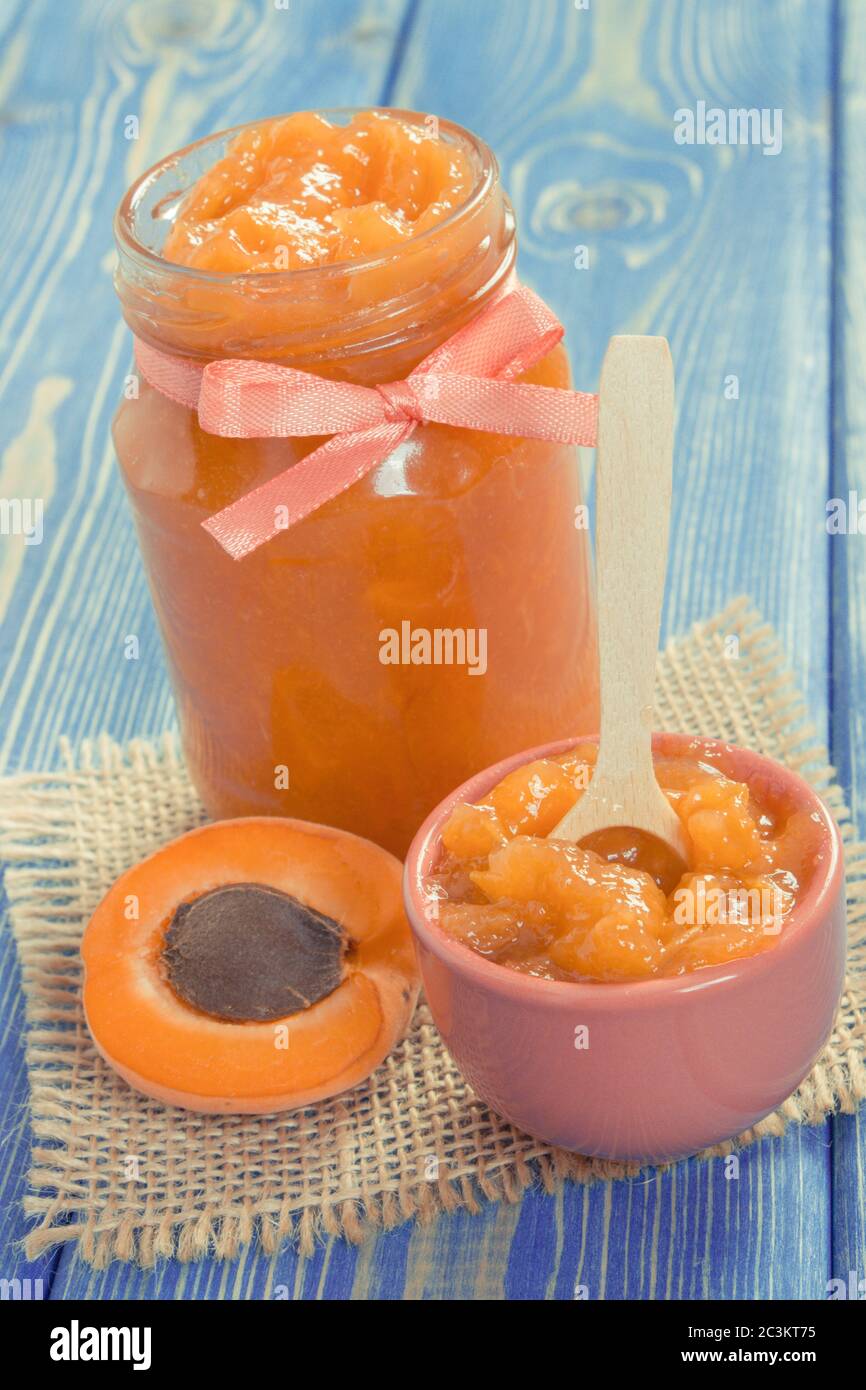 Apricot jam or marmalade in glass jar and ripe fruits on blue boards, concept of healthy sweet dessert Stock Photo