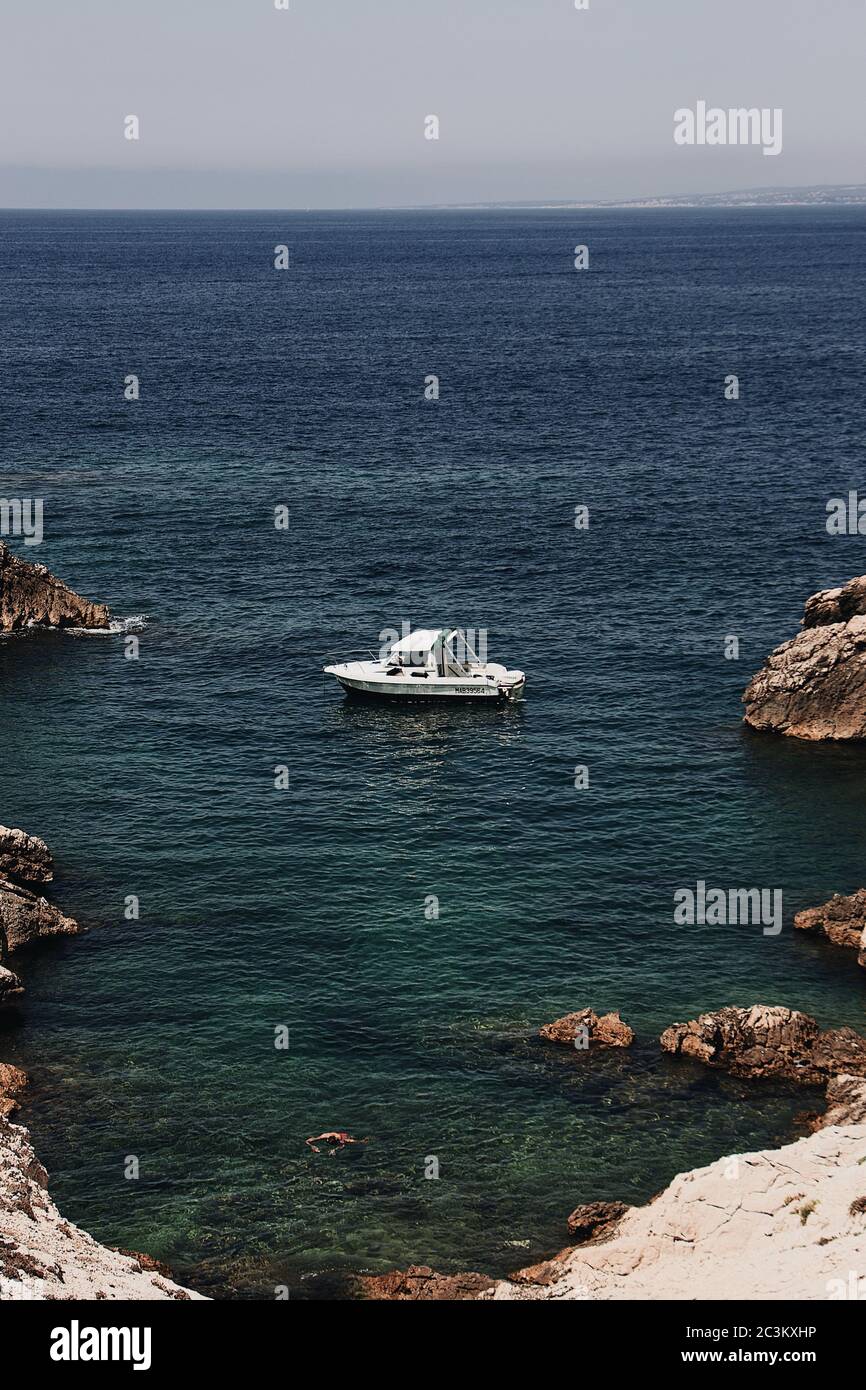 Vertical high angle shot of a boat sailing near the rocks in the blue ...