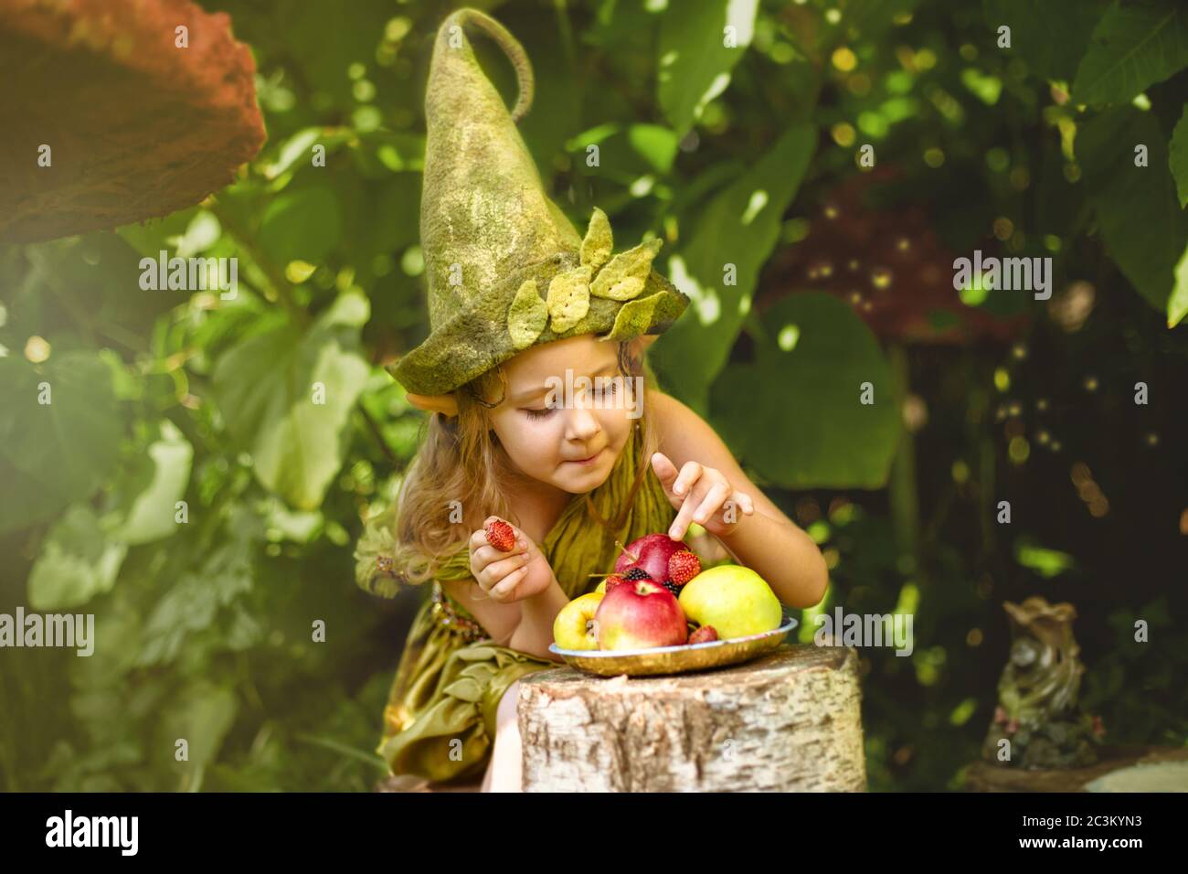 Download Portrait Of A Cute Pretty Girl In A Gnome And Costume Hat In A Green Forest In Summer Eats Berries And Apples On A Plate Stock Photo Alamy