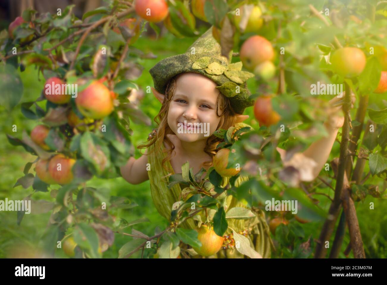 Download Portrait Of A Cute Pretty Girl In A Green Gnome Hat In A Tree With Apples Close Up Stock Photo Alamy