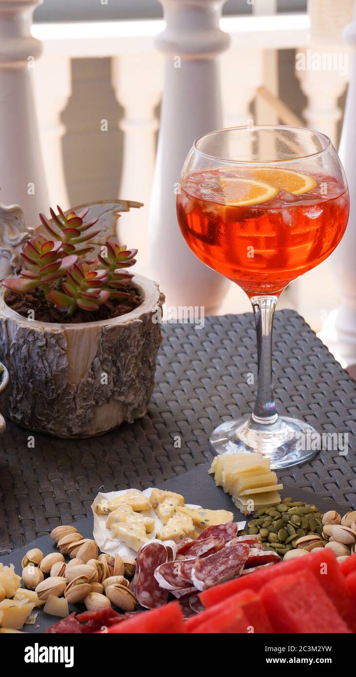 Aperol spritz in big glass red summer cocktail, cheease, meat, nuts snacks served on black board, terrace party. High quality photo Stock Photo