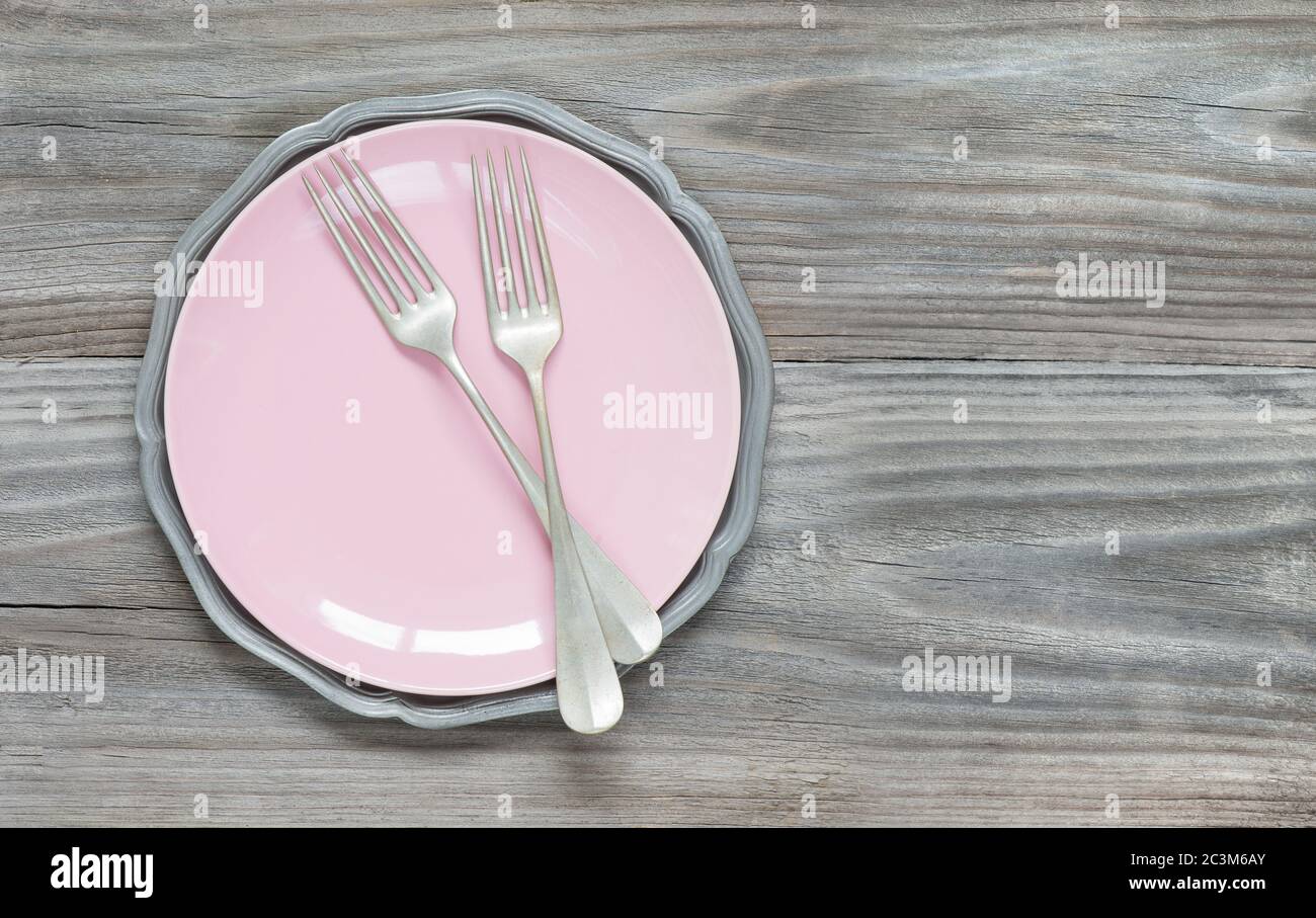 Two vintage forks on an empty pink plate on an old gray wooden