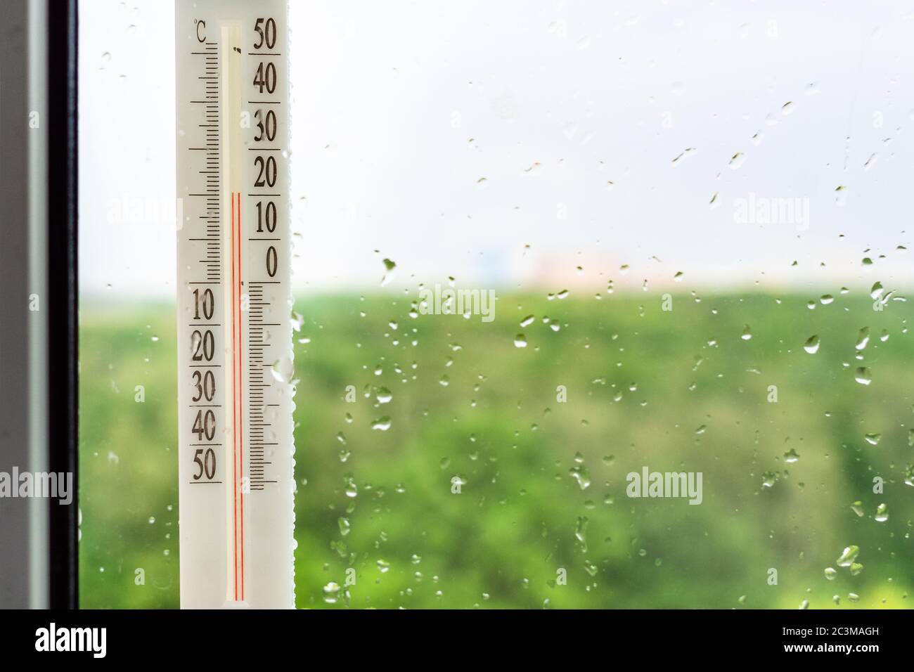 outdoor vertical thermometer on home window after rain and blurred city