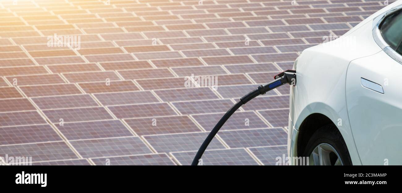 Close up of electric car with a connected charging cable on the background of solar panels and