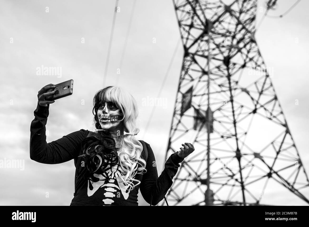 Female wearing a skeleton costume and skull makeup on her face taking a selfie of herself Stock Photo