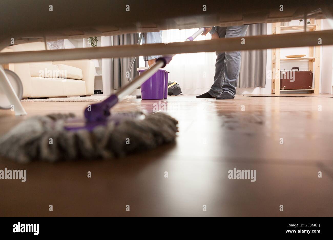 Cleaning dust under sofa while cleaning the apartment floor Stock Photo