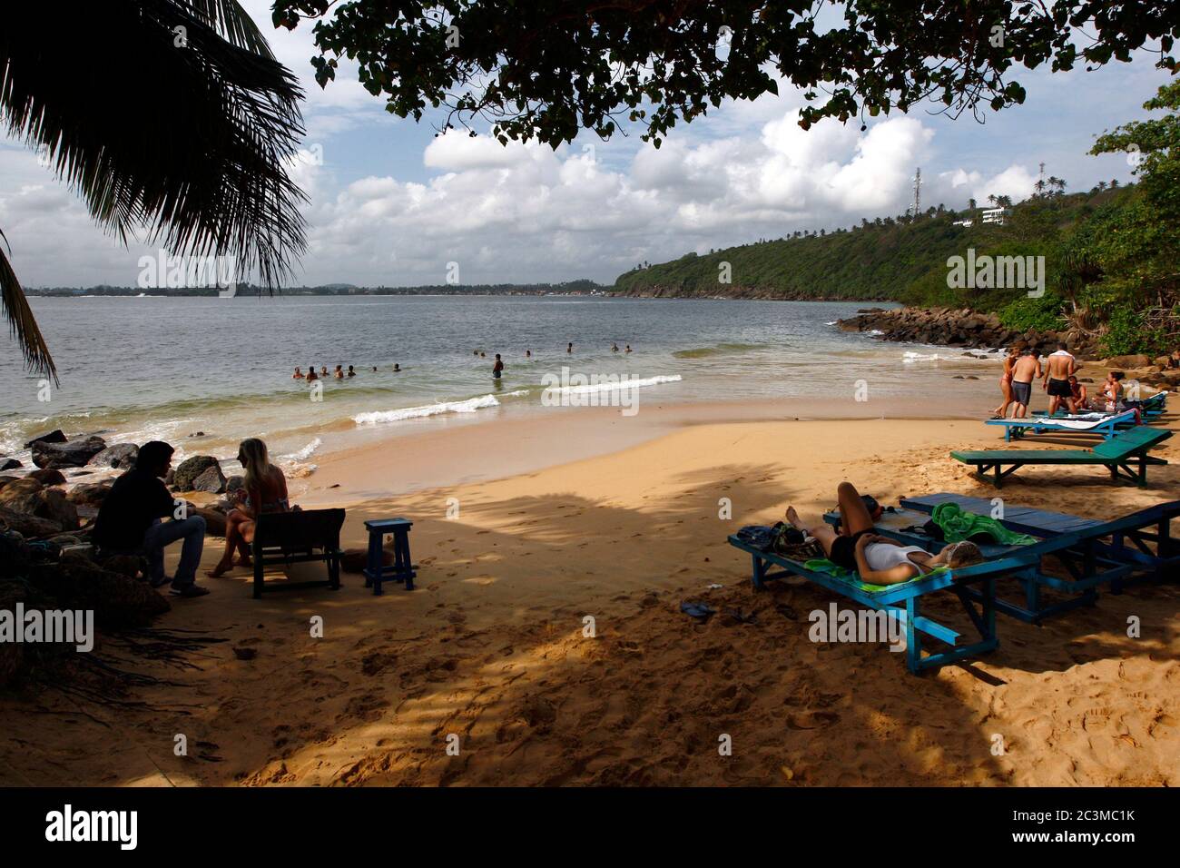 Visitors relax under the trees at Jungle Beach at Unawatuna. This beach is one of the safest swimming beaches in southern Sri Lanka. Stock Photo