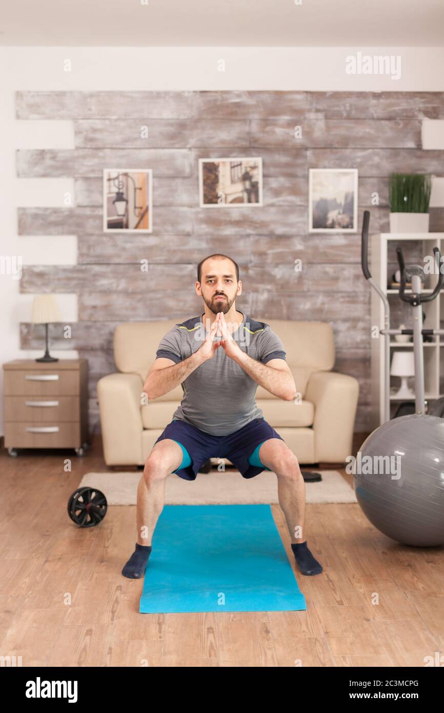 Fit man training his legs on yoga mat during global pandemic. Stock Photo