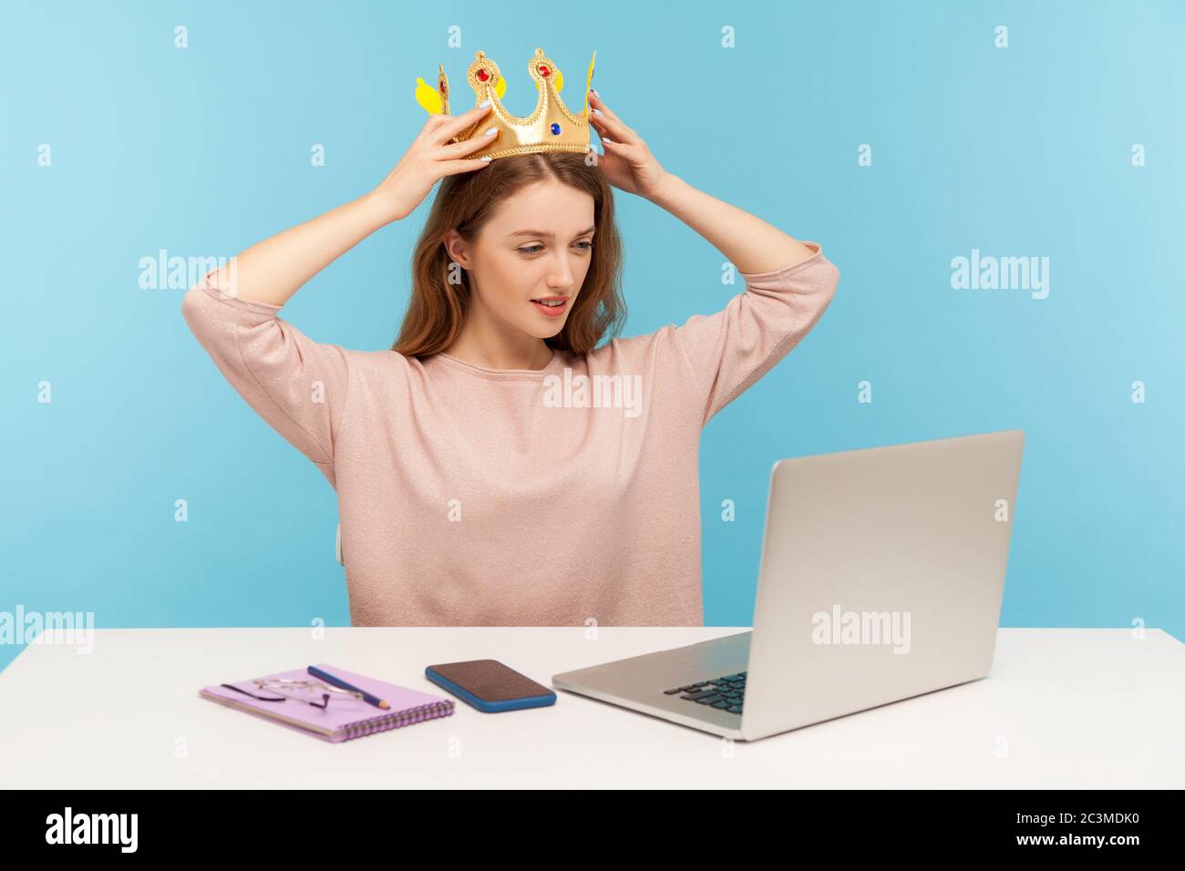 I am best queen. Arrogant self-confident ambitious businesswoman putting crown on head and looking at laptop screen, sitting in her office workplace. Stock Photo