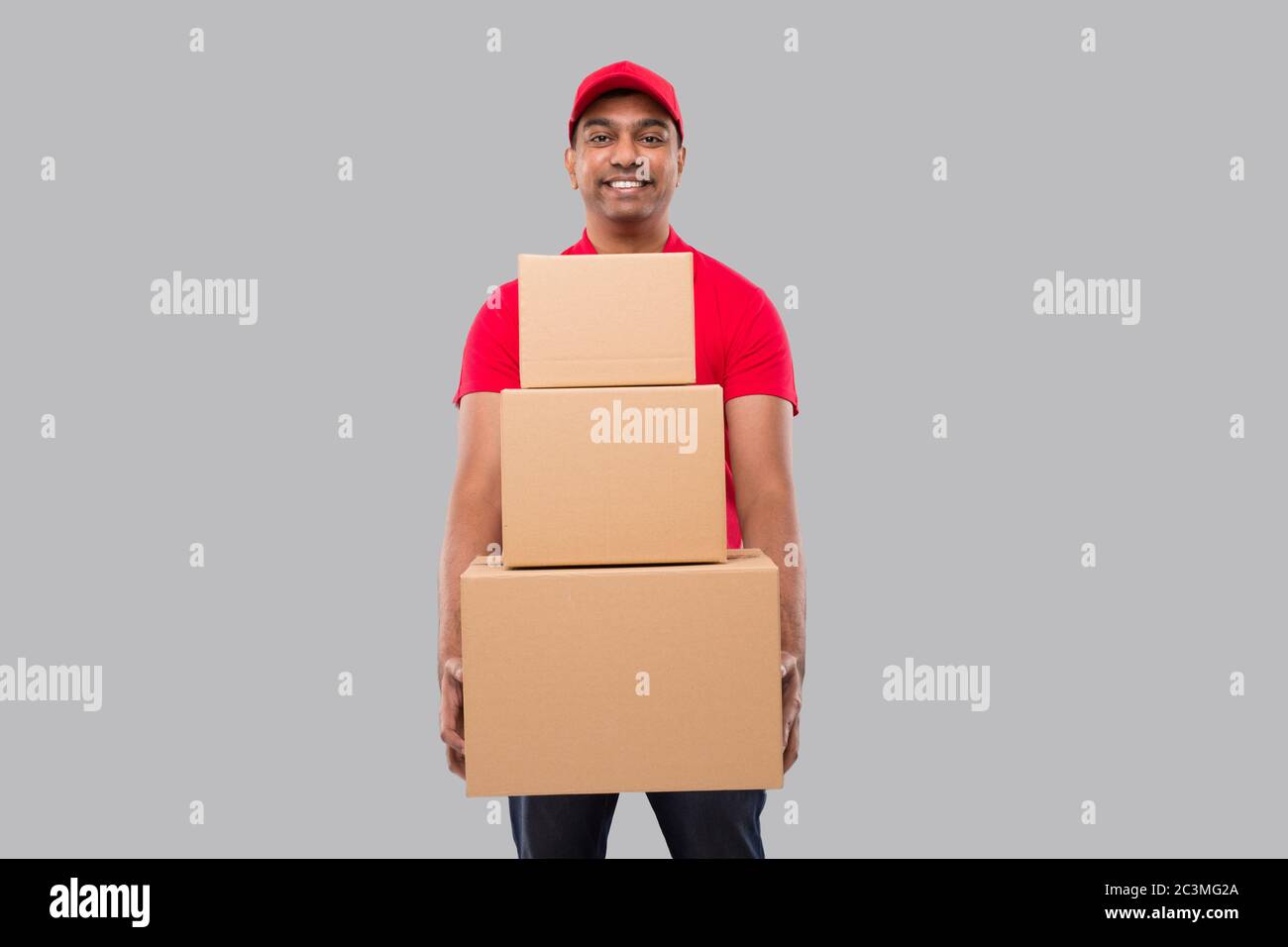 Delivery Man Holding Carton Boxes Isolated. Indian Delivery Boy Smiling with Boxes in Hands Stock Photo