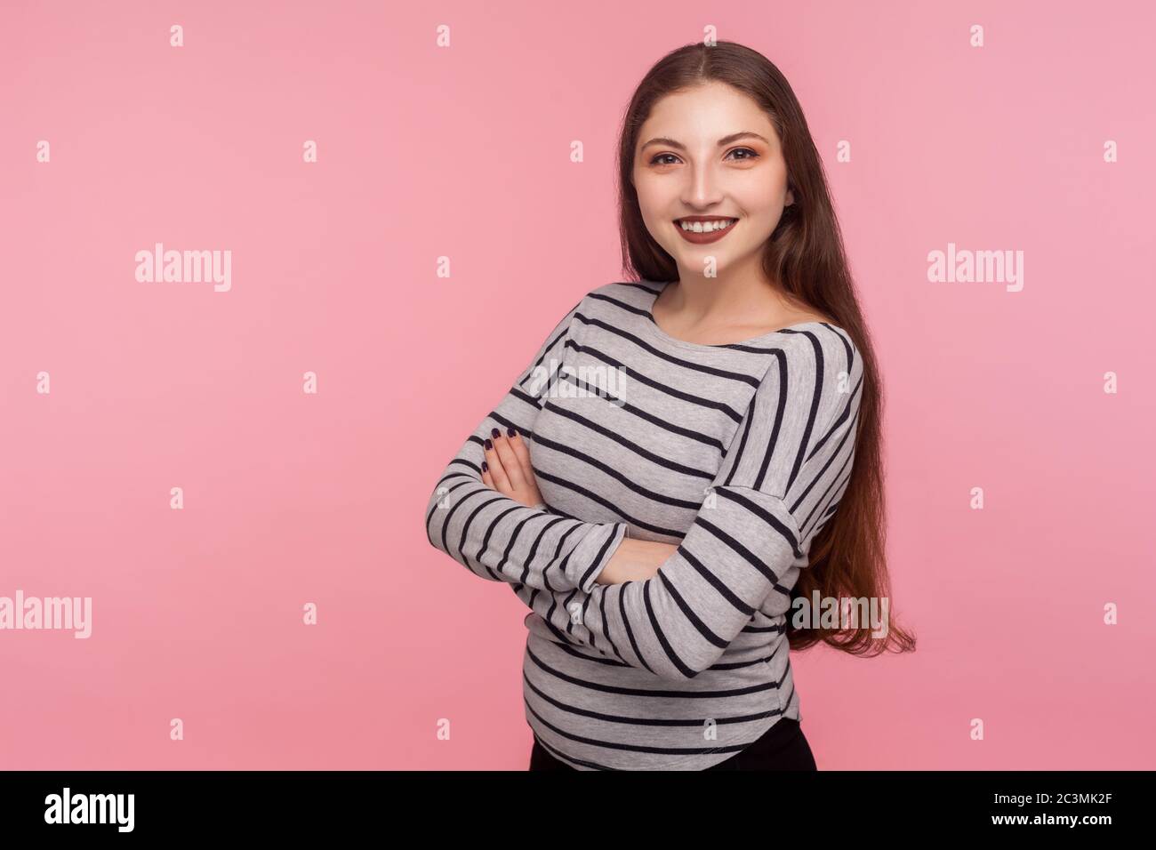 Portrait of joyful self-assured woman in striped sweatshirt looking at camera with toothy smile, crossing hands and feeling confident, satisfied with Stock Photo