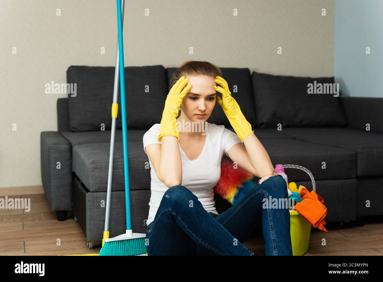 A beautiful woman in rubber gloves next to a coat and cleaning products gets angry at a lot of household chores. Problems of distribution of household Stock Photo