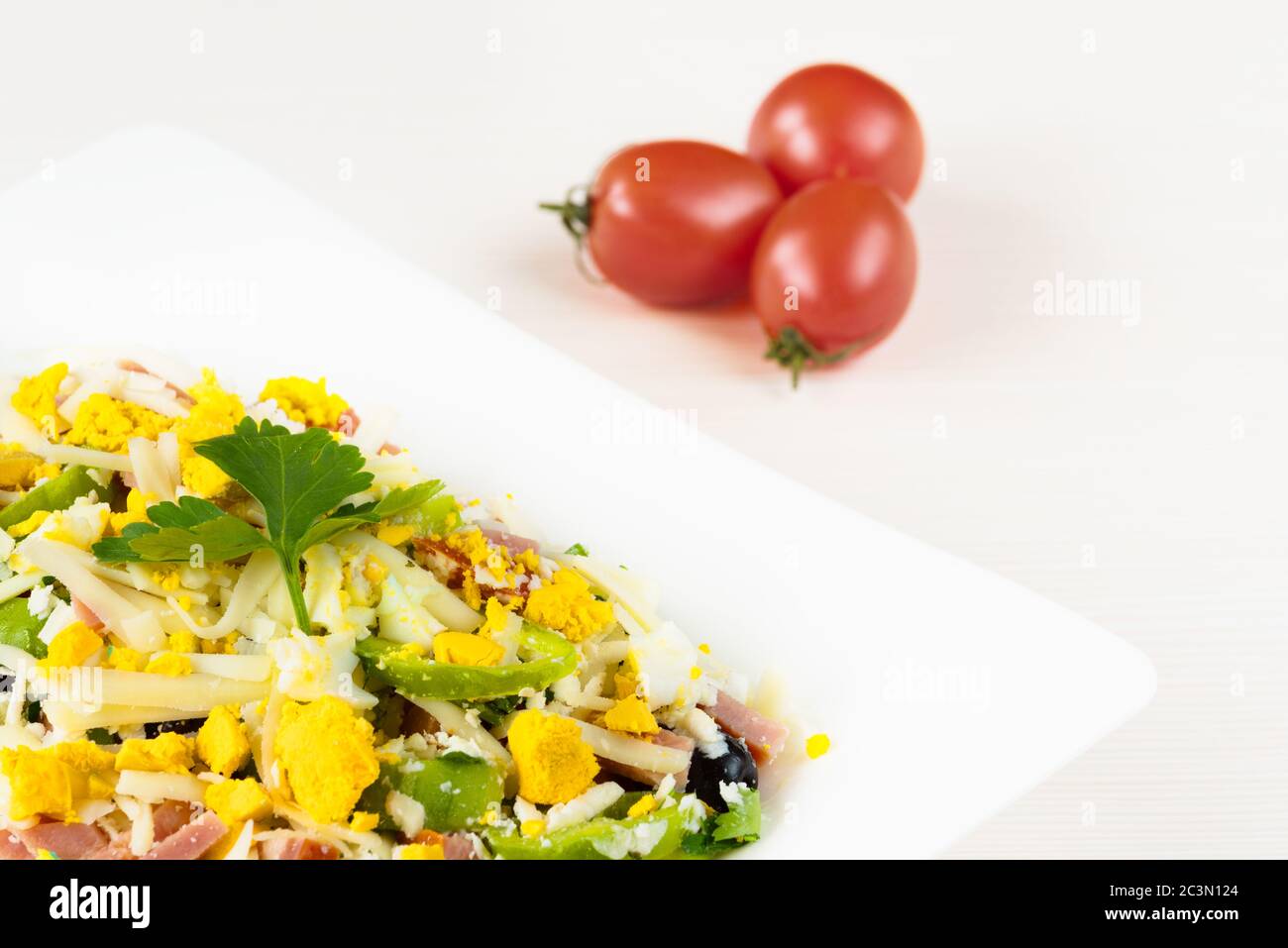 Traditional Bulgarian Shepherd salad with tomatoes, peppers, cucumbers, mushrooms, ham, cheese and eggs in white dish on white wooden table. Bulgarian Stock Photo