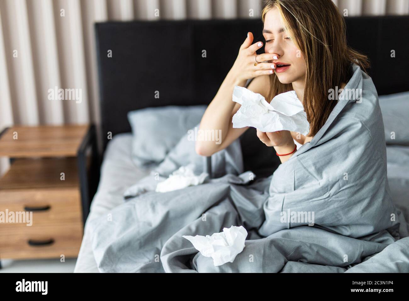 Sick woman froze and caught a cold from an unheated flat covered with warm blanket sit in bed drinking cup with hot beverage or medicines using handke Stock Photo