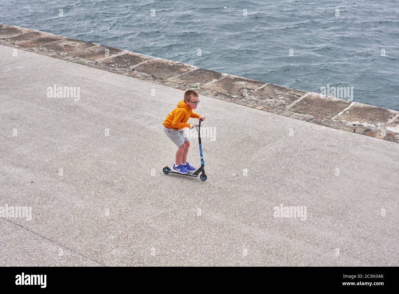 A boy on riding a scooter on Dun Laoghaire pier in Dublin city, Ireland. Stock Photo