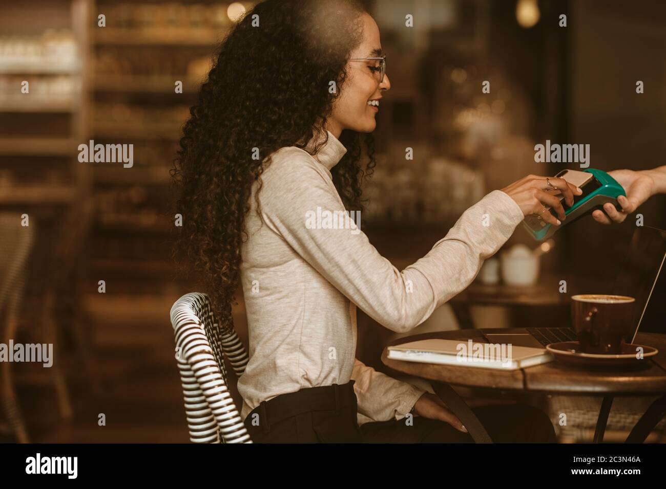 Woman at cafe paying her bill using a mobile phone and an electronic reader. Female customer paying using NFC technology in a cafe. Stock Photo