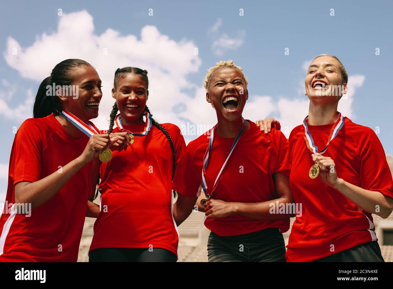 Woman football team with medals celebrating a win. Excited woman soccer team shouting in joy after winning the championship. Stock Photo