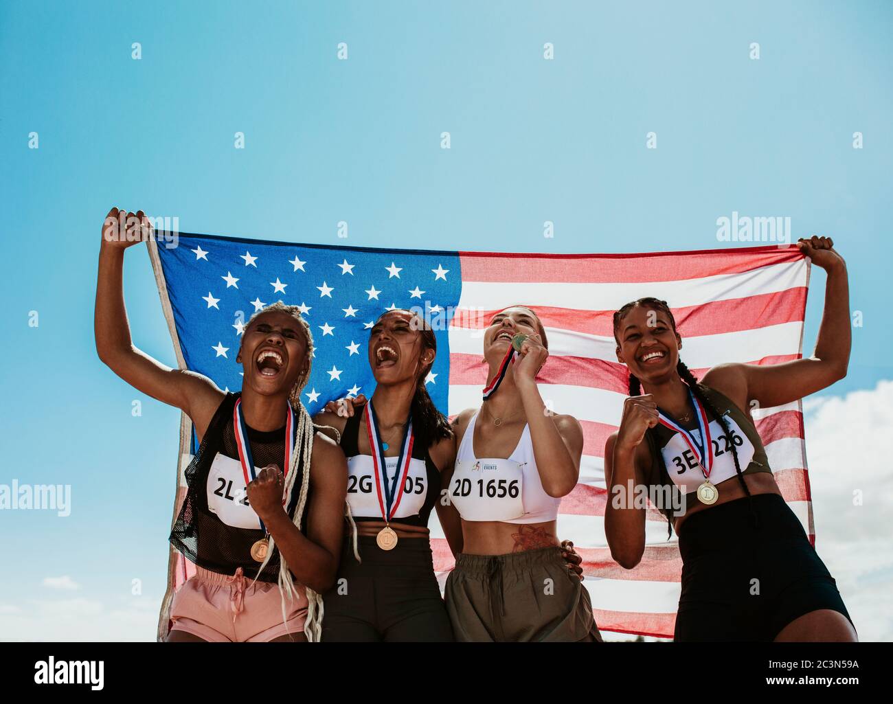 Group of four US athletes with national flag. Women runners with medals standing together holding American national flag. Stock Photo