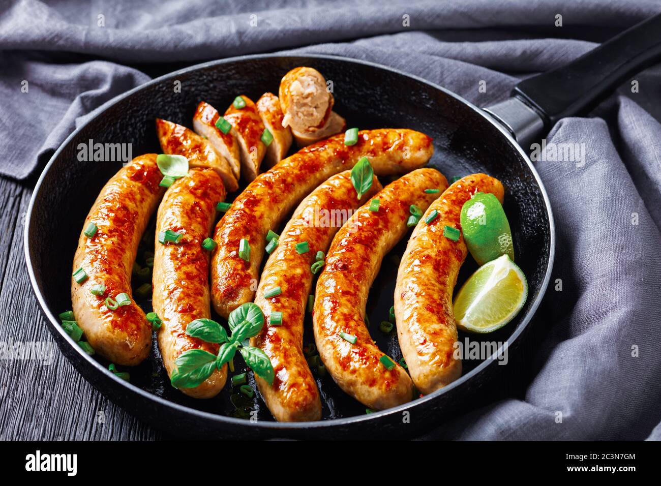 Homemade breakfast pork sausage links or patties fried in frying pan, served with fresh basil and spring onion served on a dark wooden background, lim Stock Photo
