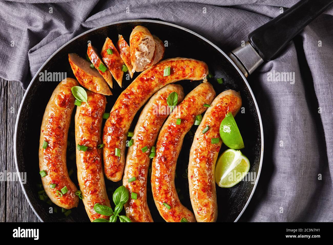 Breakfast pork sausage links or patties fried on a skillet with fresh basil and spring onion served on a dark wooden background with cutlery, lime wed Stock Photo