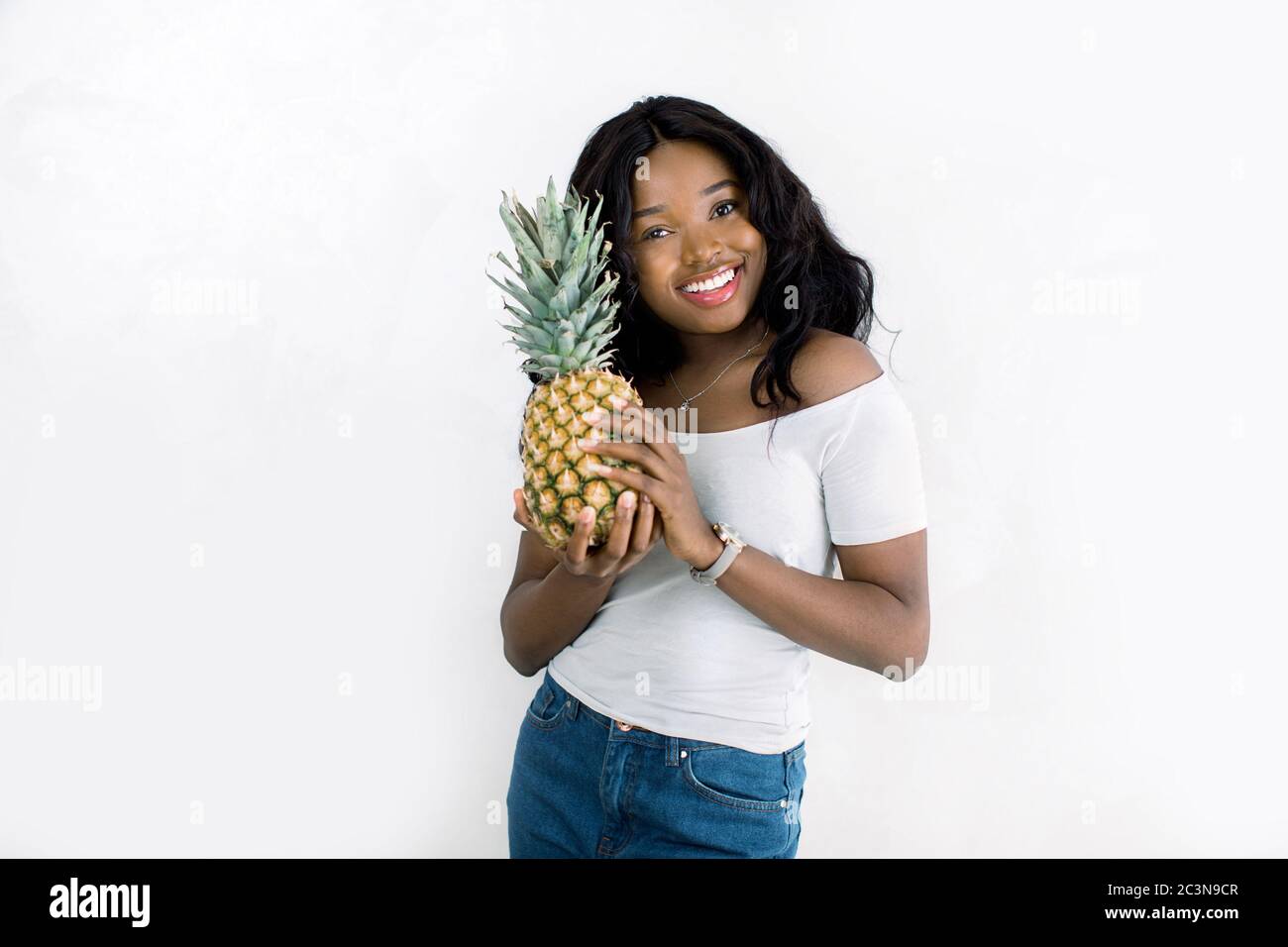 Cheerful attractive african american young woman in jeans and white t-shirt  standing and holding pineapple over white background. Beautiful African  Stock Photo - Alamy