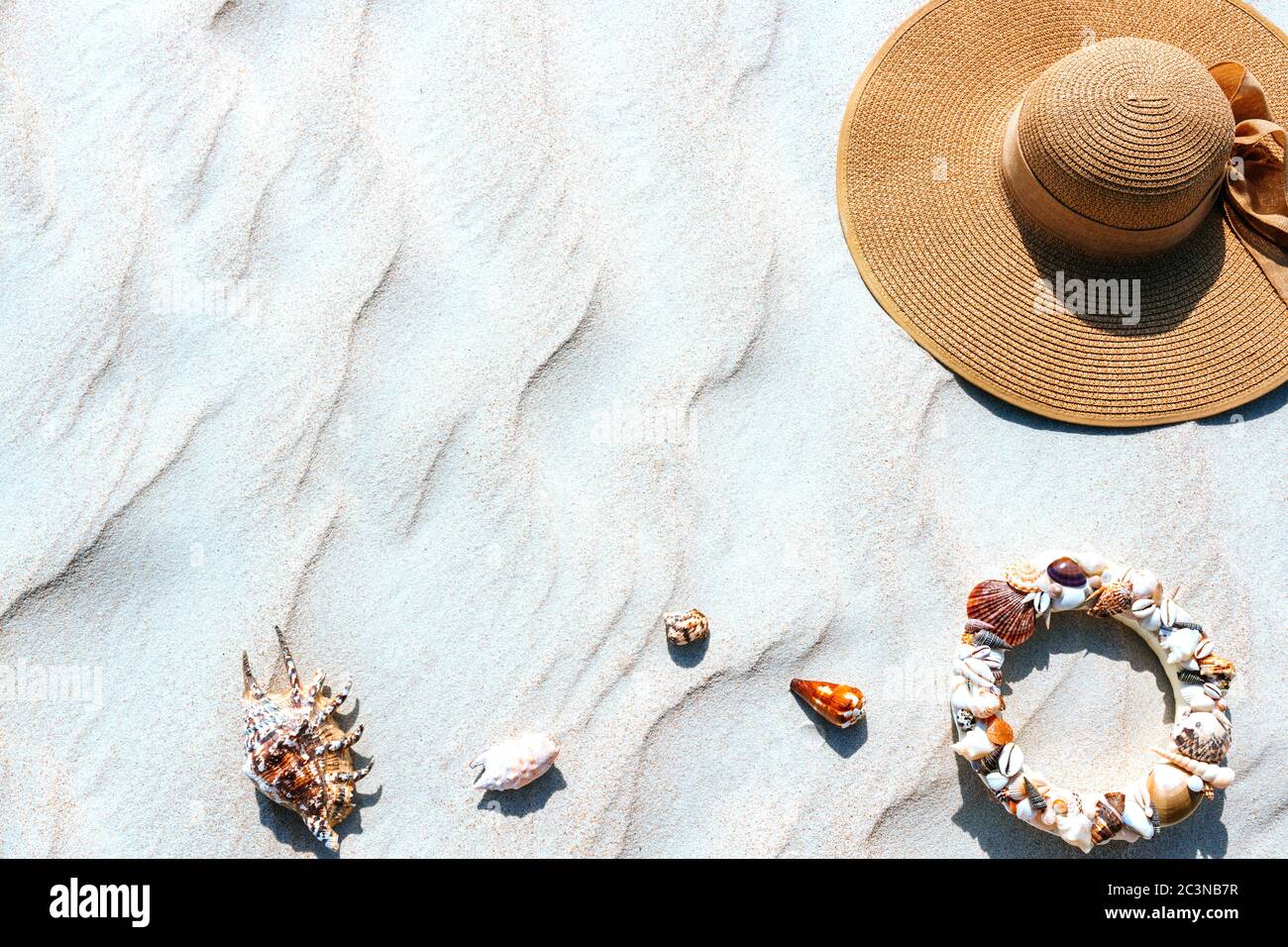Top view of a straw hat with seashells on the shore of a sandy white ...