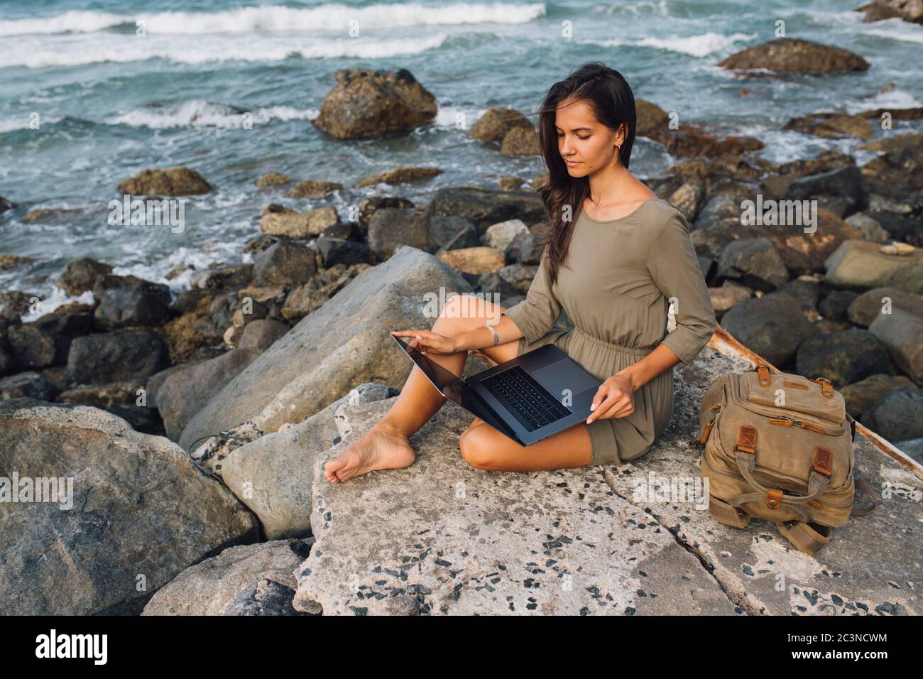 Young woman blogger working remotely with a laptop using the internet, on the seashore, sitting on the beach. Work on vacation while traveling. Freela Stock Photo