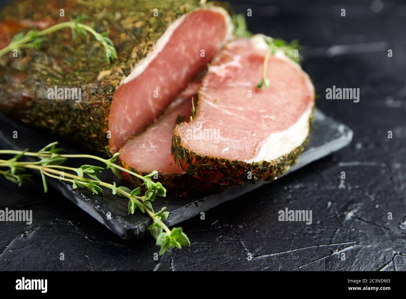 Gerky pork with spices, fresh green thyme, slate cutting board on black stone table. Polendwitz is a jerky tenderloin. Sun-dried filet, selective focu Stock Photo