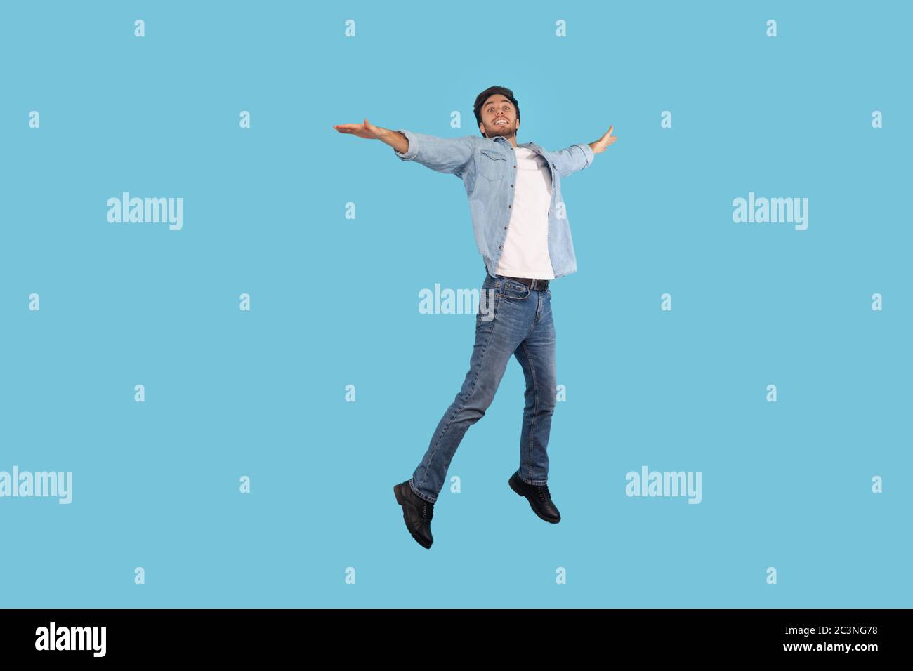 Full length, man in jeans outfit flying up in air, jumping high on trampoline with joyful expression, feeling freedom, energy, full of enthusiasm. ind Stock Photo
