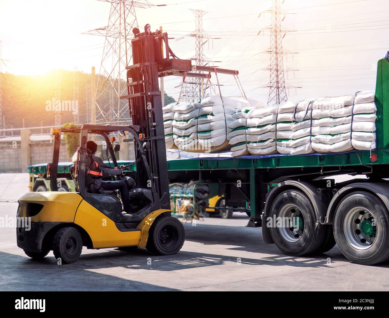 Forklift handling white sugar bags outside warehouse for stuffing onto truck. Stock Photo