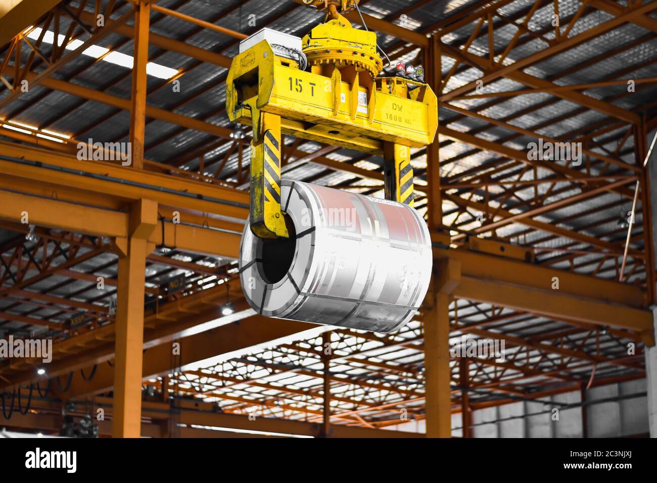 Overhead crane lift up steel coil with tong in warehouse. Steel coils handling equipment. Steel warehouse and logistics operations. Stock Photo