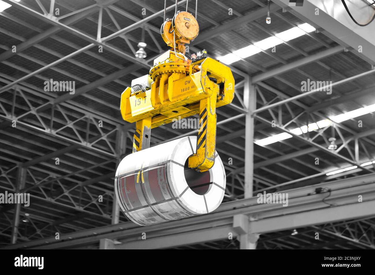 Overhead crane lift up steel coil with tong in warehouse. Steel coils handling equipment. Steel warehouse and logistics operations. Stock Photo