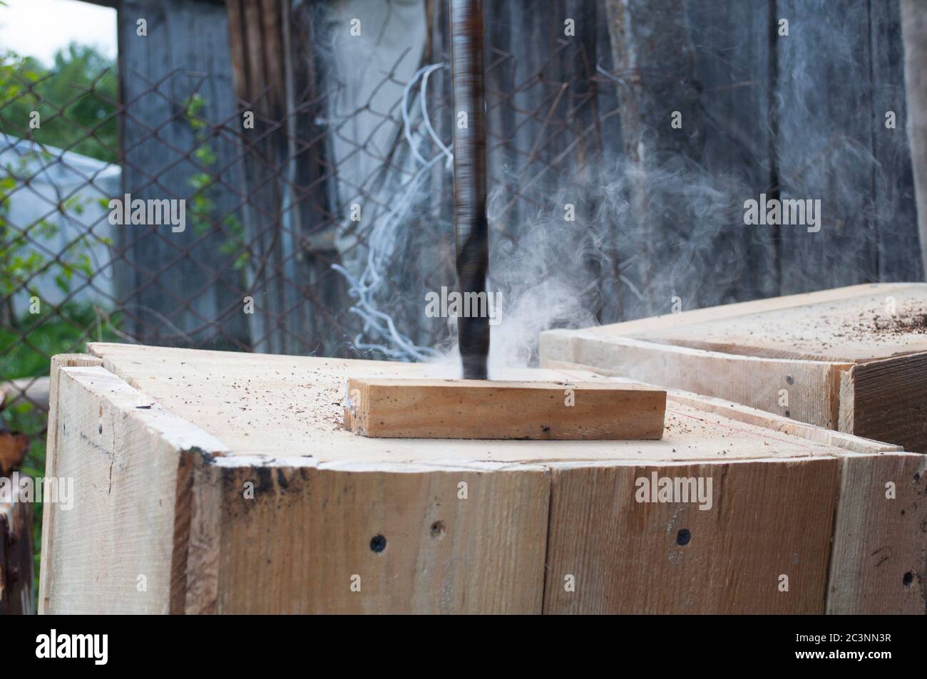 Drilling a hole in a wooden board at high speed there is smoke Stock Photo
