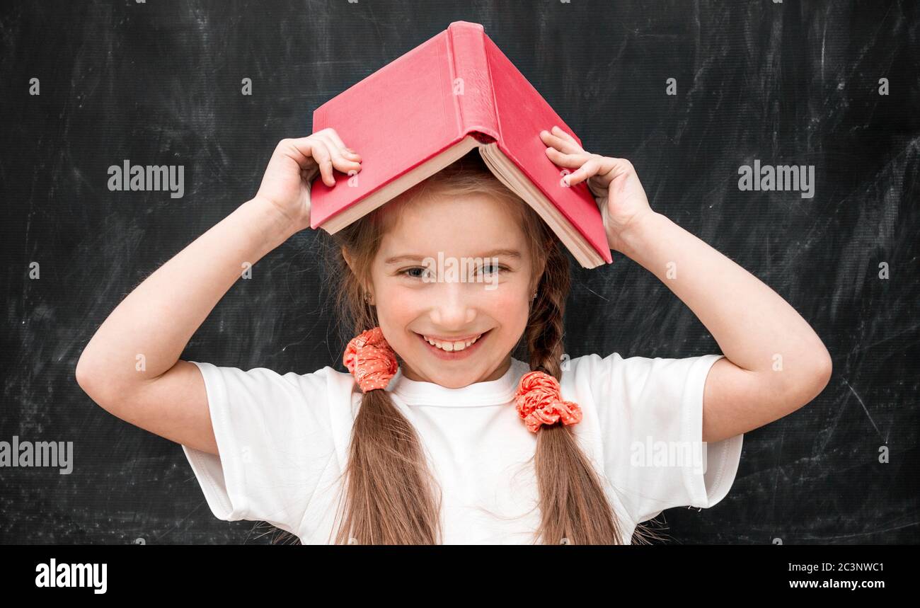cute little girl with a red book on her head smiling in school Stock ...