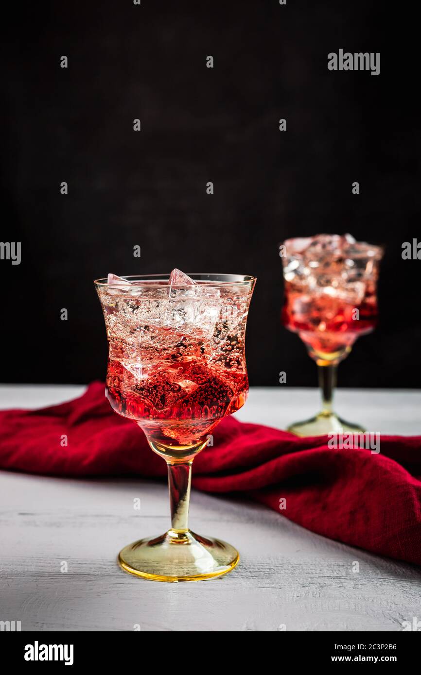 Two beautiful refreshing sparkling cocktails with ice, white wooden table, dark background, red napkin Stock Photo