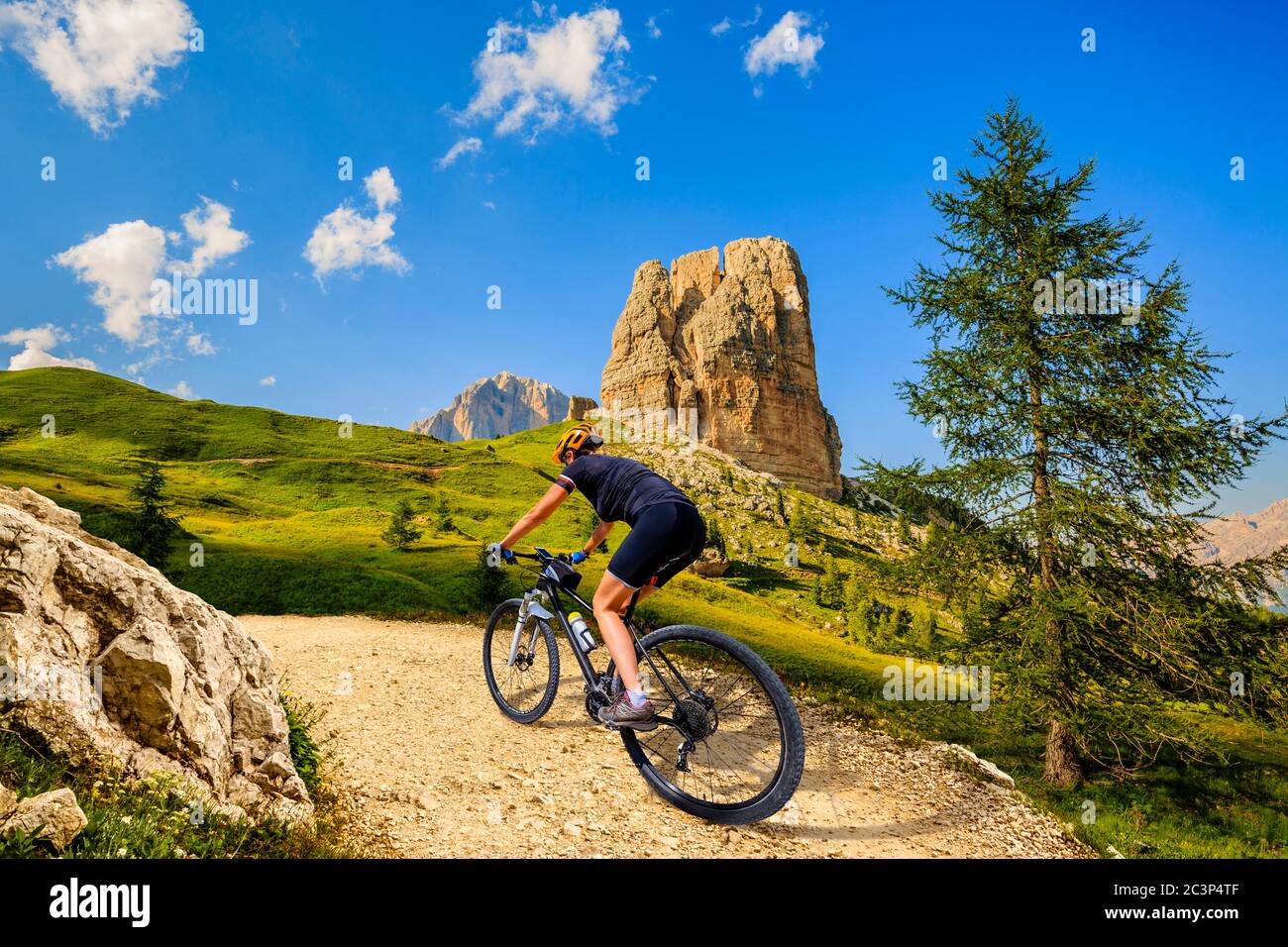 Woman cycling in Cortina d'Ampezzo, stunning Cinque Torri and Tofana in background. Woman riding MTB trail. South Tyrol province of Italy, Dolomites. Stock Photo