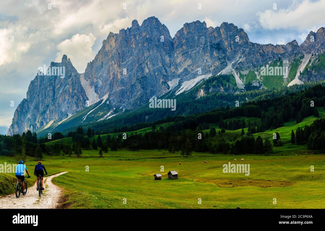 Couple cycling in Cortina d'Ampezzo, stunning Dolomites mountains in background. Woman and man riding MTB trail. South Tyrol province of Italy, Dolomi Stock Photo