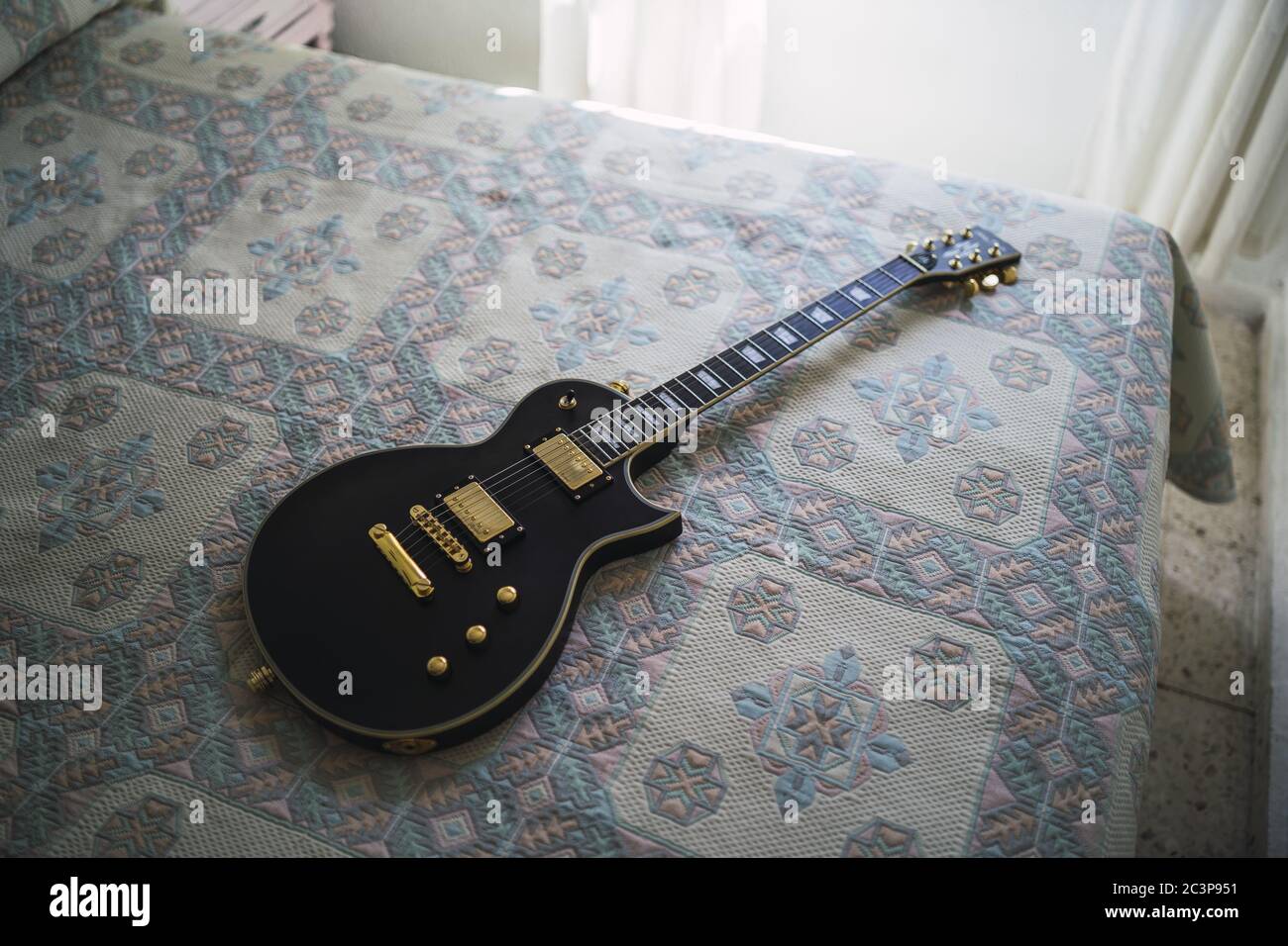 High angle shot of a black electric guitar on a bed with patterned sheet Stock Photo