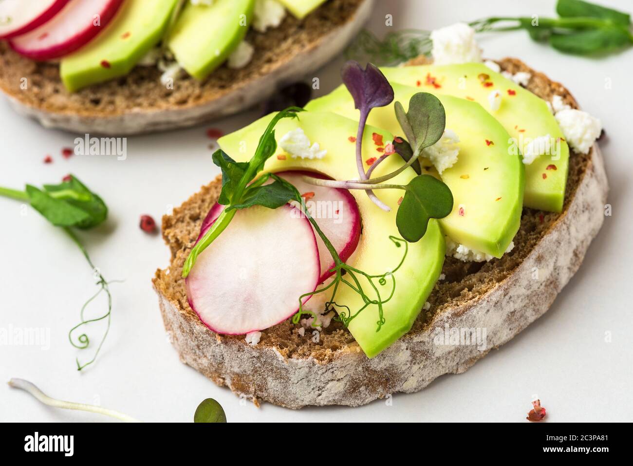 Avocado toasts with radish, feta cheese, sprouts and pepper for breakfast on white marble table. healthy diet snacks. close up Stock Photo
