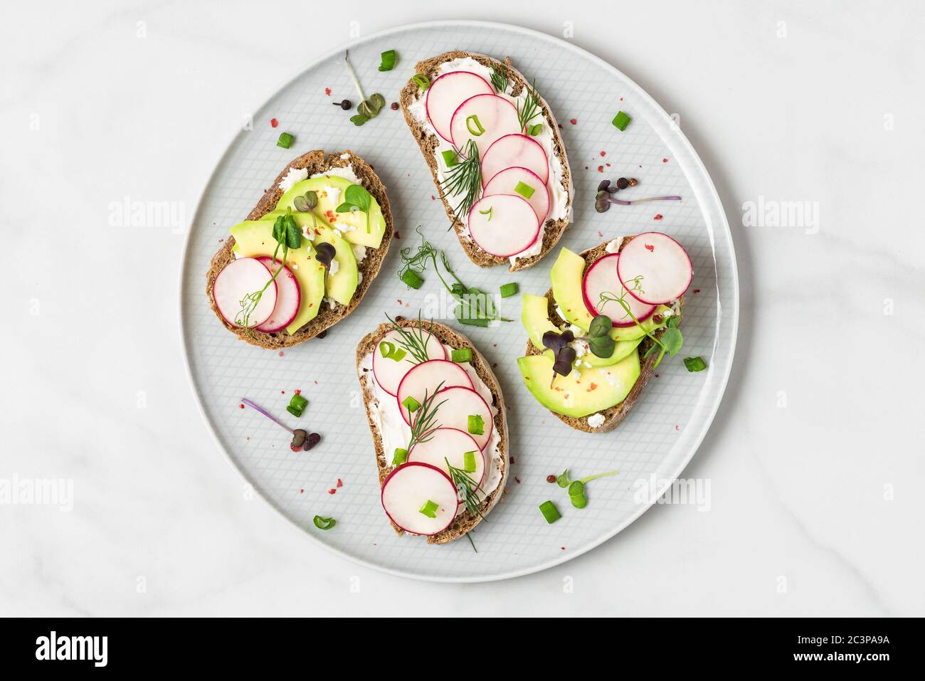 Avocado and radish toast with feta cheese, sprouts and pepper in a plate for healthy diet breakfast. top view Stock Photo