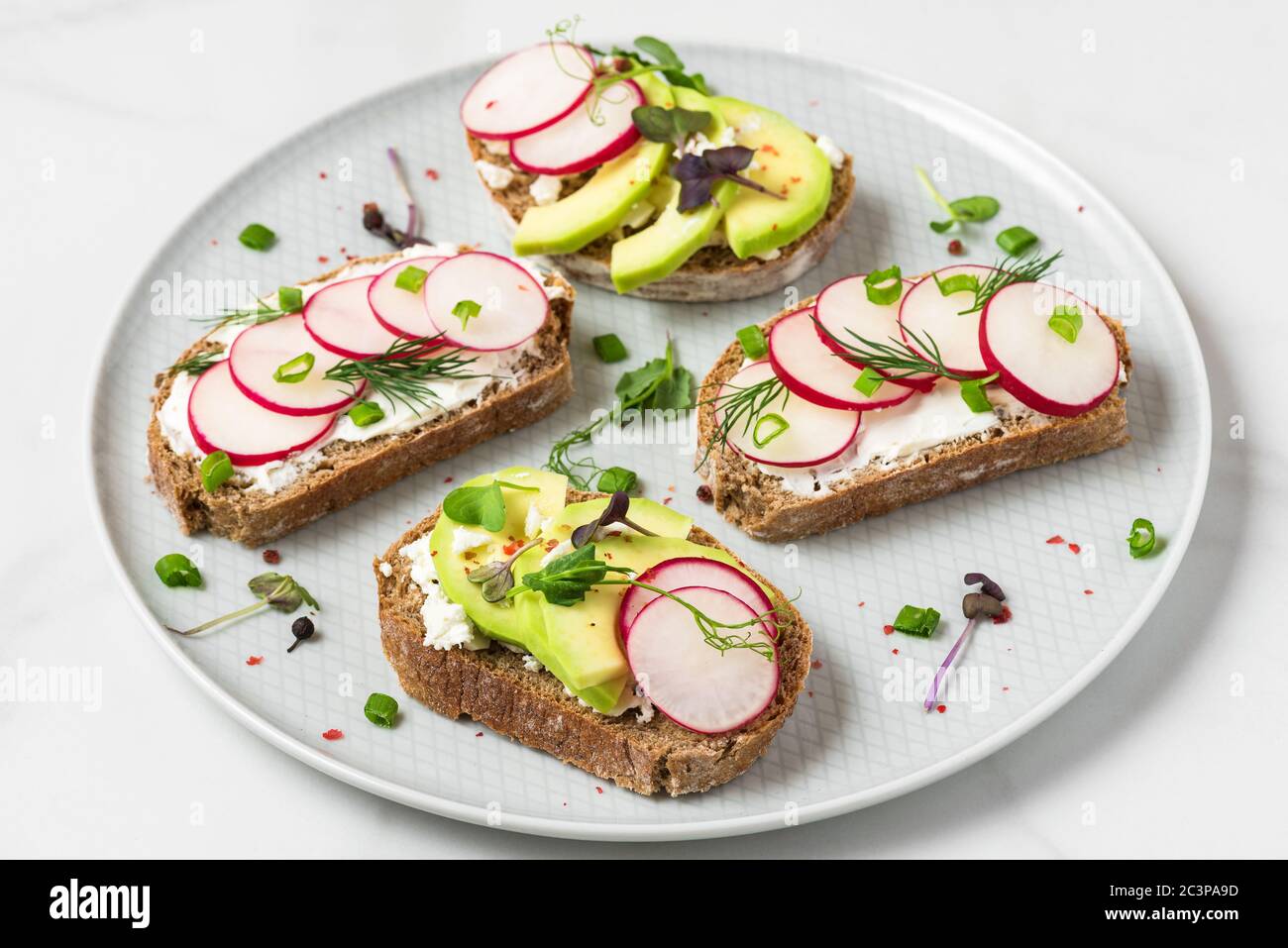 Avocado and radish toast with feta cheese, sprouts and pepper in a plate for healthy breakfast. close up Stock Photo