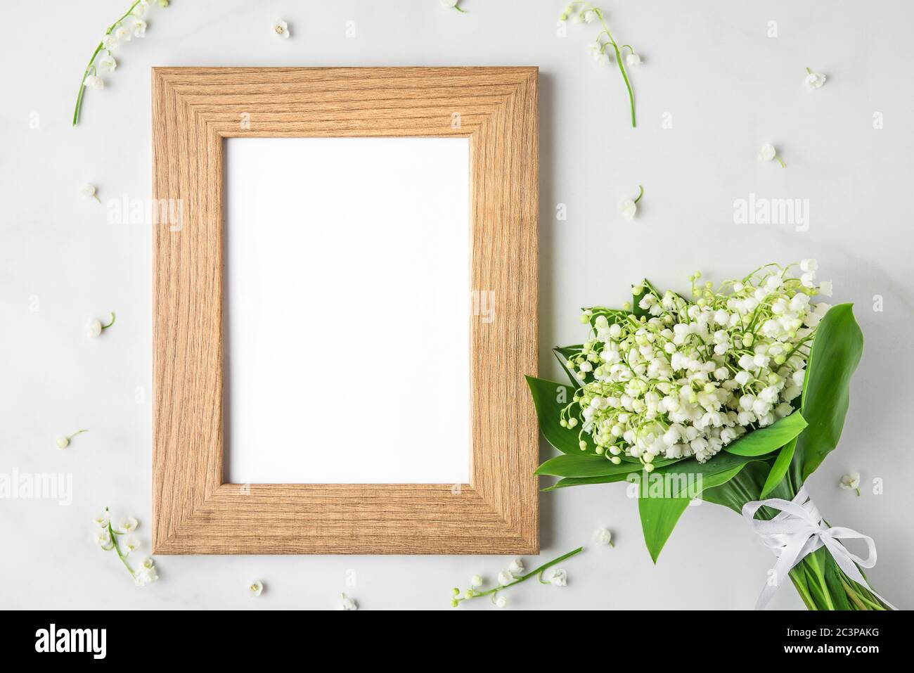 blank photo frame with lily of the valley flowers bouquet on white background. mock up. flat lay. top view. wedding or festive concept Stock Photo