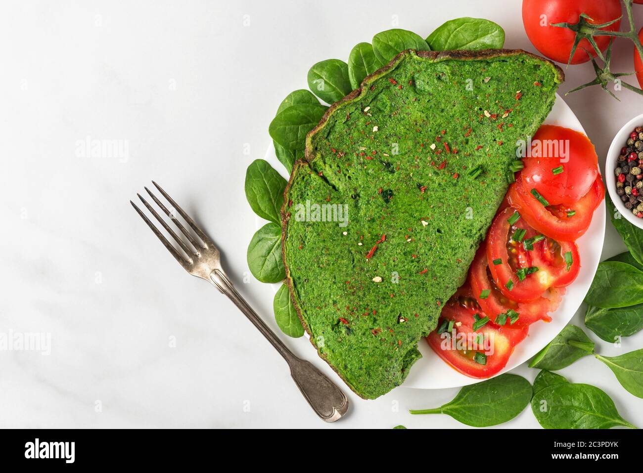 Healthy green spinach omelette with fresh tomatoes, spices, herbs and fork on white background. ketogenic diet food. top view with copy space Stock Photo
