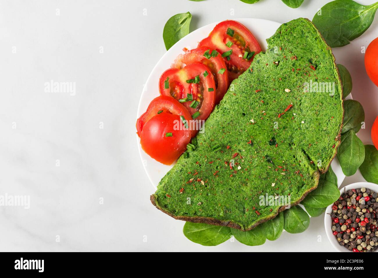 Healthy green spinach omelette with fresh tomatoes, spices and herbs on white background. ketogenic diet food. top view with copy space Stock Photo